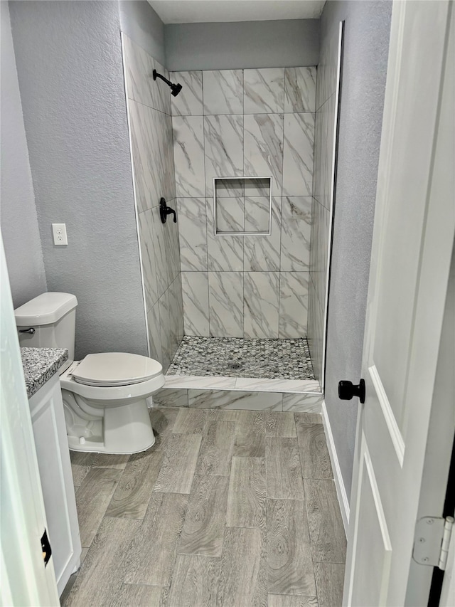 bathroom with hardwood / wood-style floors, tiled shower, toilet, and vanity