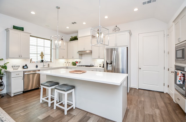 kitchen with white cabinetry, appliances with stainless steel finishes, pendant lighting, hardwood / wood-style flooring, and a center island