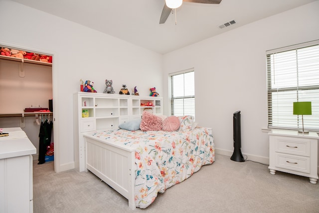 carpeted bedroom with ceiling fan, multiple windows, a closet, and a walk in closet