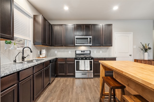 kitchen with sink, stainless steel appliances, dark brown cabinetry, decorative backsplash, and light wood-type flooring