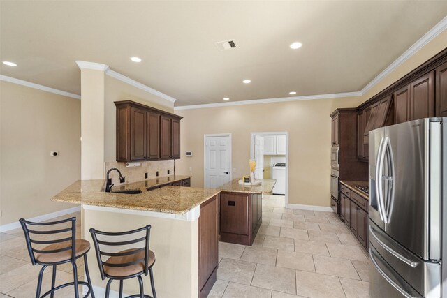 kitchen featuring stainless steel appliances, washer / clothes dryer, sink, a kitchen breakfast bar, and kitchen peninsula