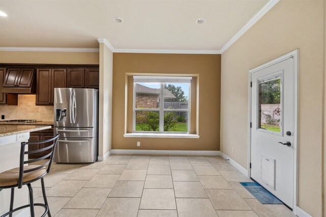 kitchen featuring light stone counters, stainless steel refrigerator with ice dispenser, dark brown cabinetry, light tile patterned floors, and tasteful backsplash