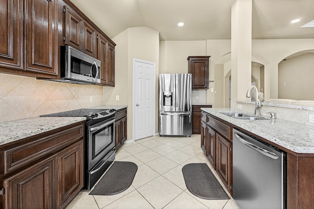 kitchen with stainless steel appliances, sink, light tile patterned floors, backsplash, and dark brown cabinets