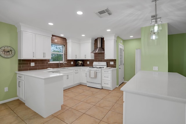 kitchen with wall chimney range hood, white range, kitchen peninsula, pendant lighting, and white cabinets