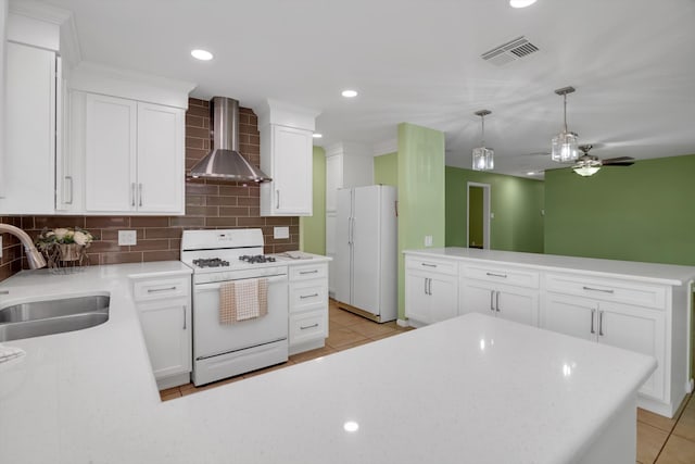 kitchen with white appliances, wall chimney range hood, sink, ceiling fan, and white cabinetry