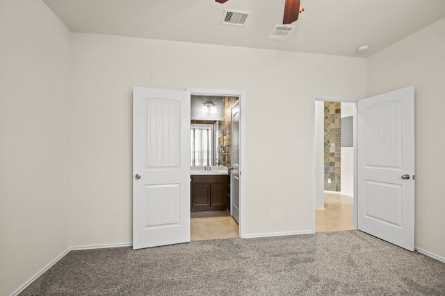 unfurnished bedroom featuring sink, light carpet, ceiling fan, and ensuite bath