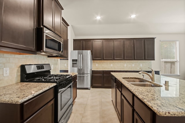 kitchen featuring stainless steel appliances, sink, backsplash, and light stone countertops