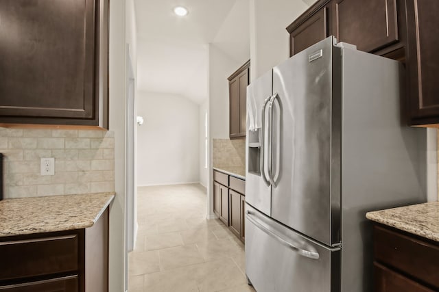 kitchen with light tile patterned floors, light stone countertops, stainless steel refrigerator with ice dispenser, decorative backsplash, and vaulted ceiling