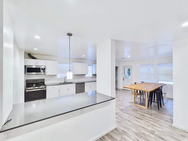 kitchen with stainless steel appliances, sink, hanging light fixtures, light hardwood / wood-style flooring, and white cabinets