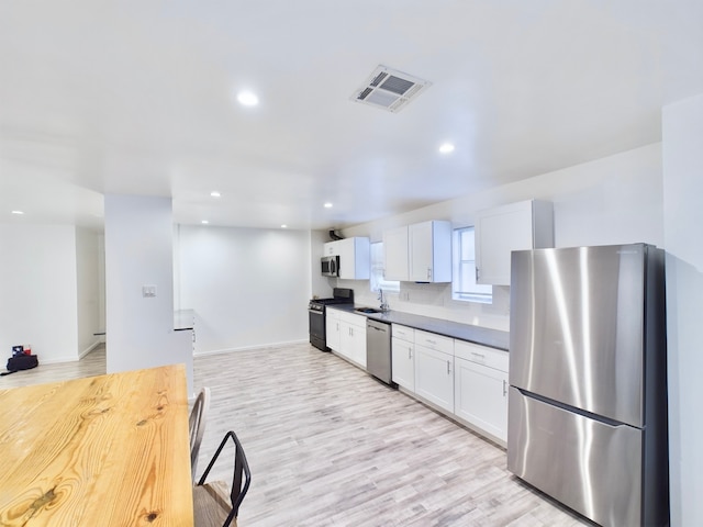 kitchen featuring sink, tasteful backsplash, white cabinetry, light wood-type flooring, and appliances with stainless steel finishes