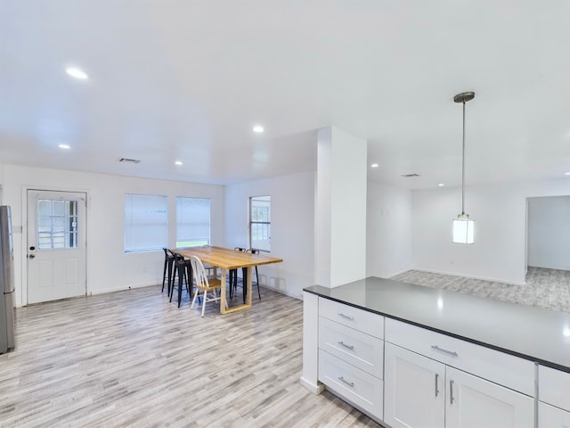 kitchen featuring light wood-type flooring, decorative light fixtures, stainless steel refrigerator, and white cabinets