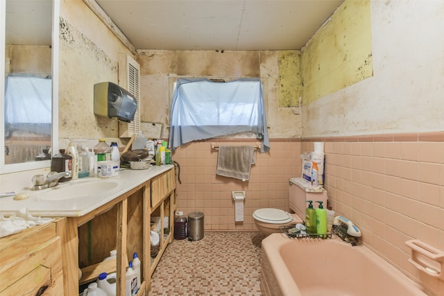 bathroom featuring a tub, vanity, toilet, and tile walls