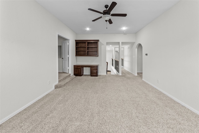 unfurnished living room featuring ceiling fan, light colored carpet, and built in desk