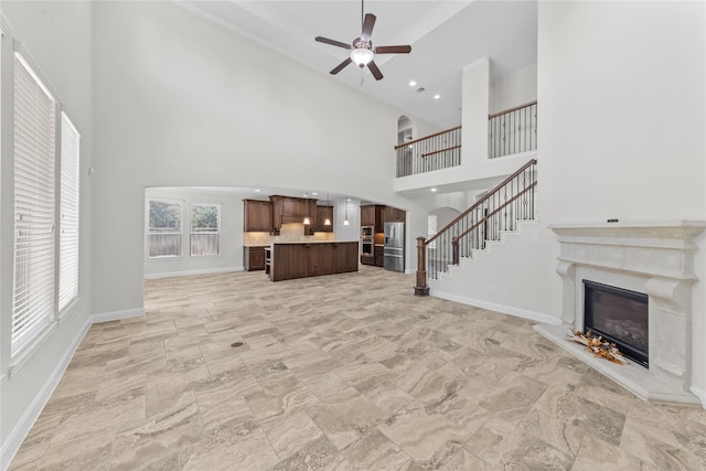 unfurnished living room featuring ceiling fan, a towering ceiling, and a fireplace