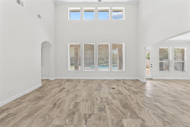 unfurnished living room featuring a towering ceiling, crown molding, and a wealth of natural light