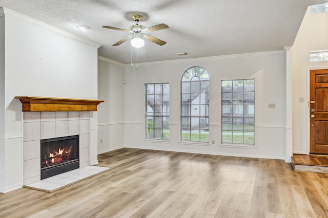 unfurnished living room with ceiling fan, a textured ceiling, light hardwood / wood-style flooring, crown molding, and a tile fireplace