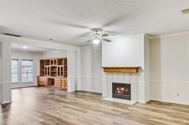 unfurnished living room with light wood-type flooring, built in desk, ornamental molding, and a fireplace