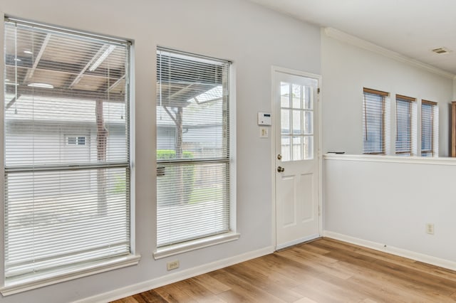 entryway with a wealth of natural light, light wood-type flooring, and crown molding