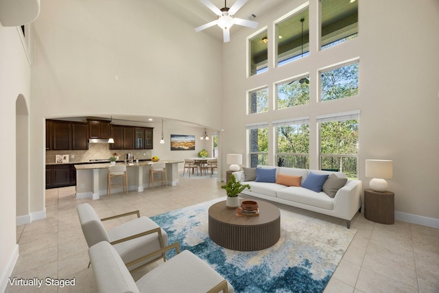 tiled living room featuring ceiling fan, sink, and a towering ceiling