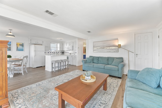 living room with sink, light wood-type flooring, and ornamental molding