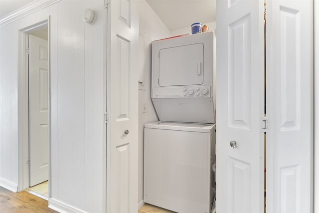 laundry area with wood walls, stacked washer and clothes dryer, and light hardwood / wood-style flooring