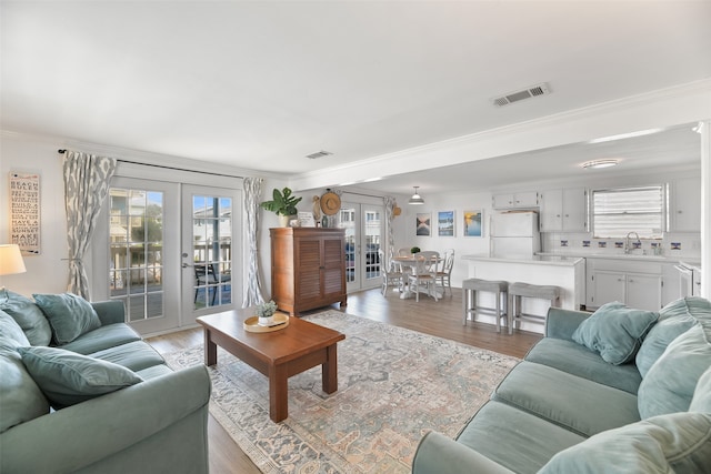 living room featuring light hardwood / wood-style floors, crown molding, sink, and french doors