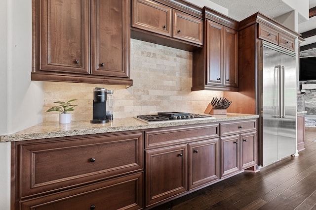 kitchen with light stone counters, dark hardwood / wood-style floors, backsplash, a textured ceiling, and appliances with stainless steel finishes