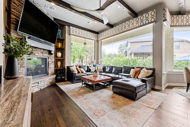 living room featuring beamed ceiling, a stone fireplace, and wood-type flooring