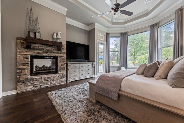 bedroom featuring ceiling fan, wood-type flooring, a tray ceiling, a fireplace, and ornamental molding