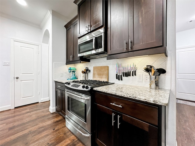 kitchen featuring dark brown cabinetry, appliances with stainless steel finishes, light stone countertops, crown molding, and dark hardwood / wood-style flooring