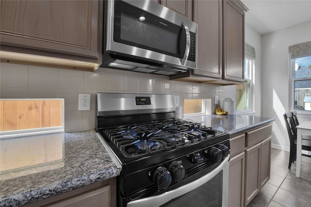 kitchen featuring stone counters, decorative backsplash, light tile patterned floors, and stainless steel appliances