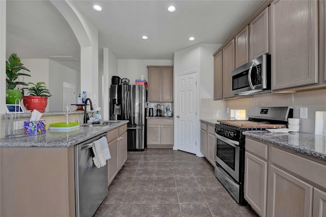 kitchen with decorative backsplash, stainless steel appliances, sink, and light stone countertops