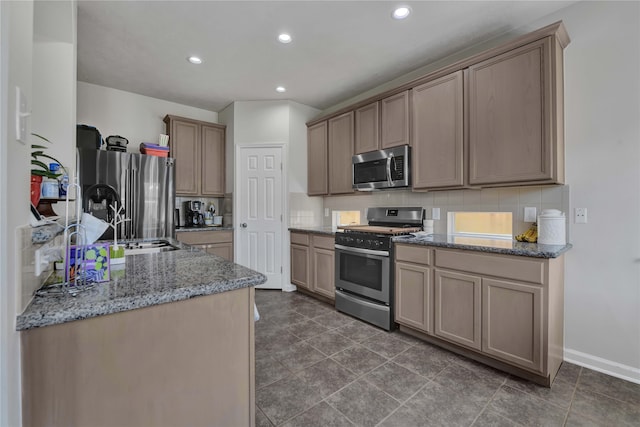 kitchen featuring tasteful backsplash, light stone counters, appliances with stainless steel finishes, dark tile patterned flooring, and sink