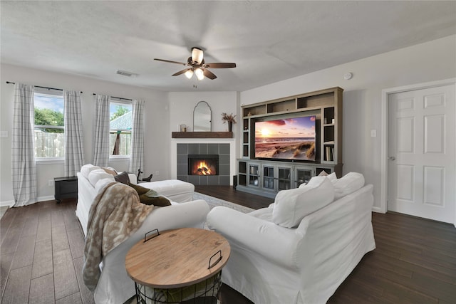 living room with ceiling fan, a tiled fireplace, a textured ceiling, and dark hardwood / wood-style floors