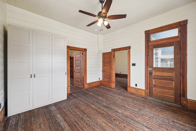 unfurnished bedroom featuring dark wood-type flooring, ceiling fan, wooden walls, and a closet