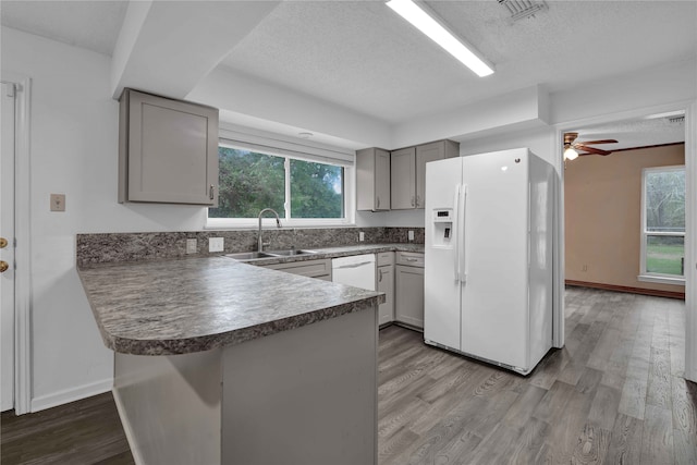 kitchen featuring a textured ceiling, white appliances, sink, a healthy amount of sunlight, and kitchen peninsula