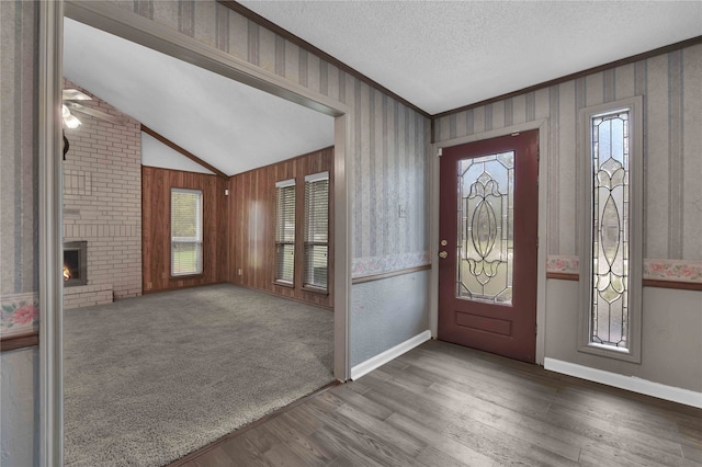 foyer entrance with a textured ceiling, hardwood / wood-style floors, a fireplace, lofted ceiling, and wooden walls