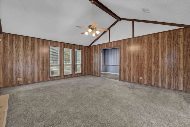 carpeted spare room featuring wood walls, ceiling fan, and vaulted ceiling with beams