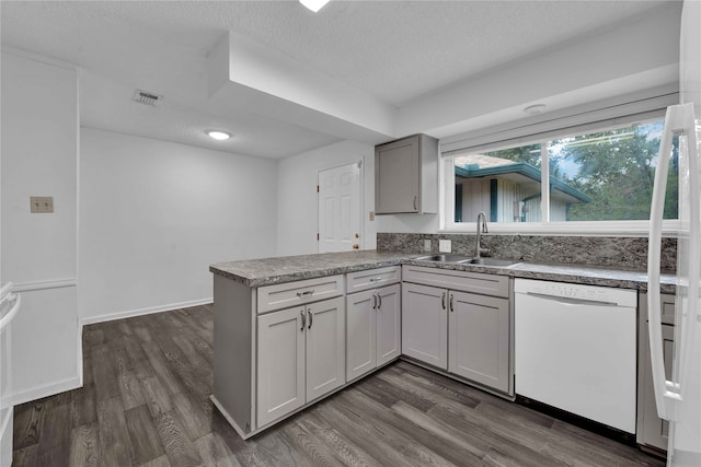 kitchen with white dishwasher, dark hardwood / wood-style flooring, sink, and kitchen peninsula