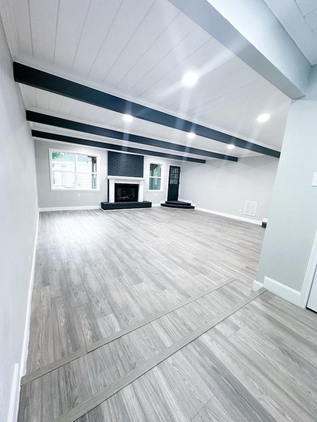 unfurnished living room featuring a large fireplace, beam ceiling, and hardwood / wood-style floors