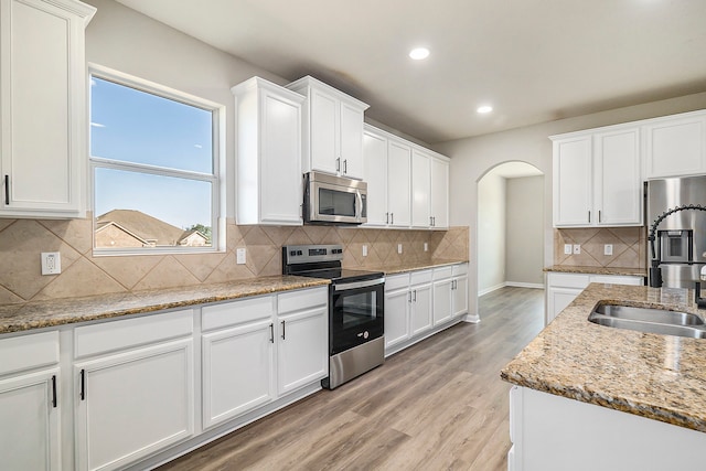 kitchen featuring light stone counters, light wood-type flooring, appliances with stainless steel finishes, backsplash, and white cabinets