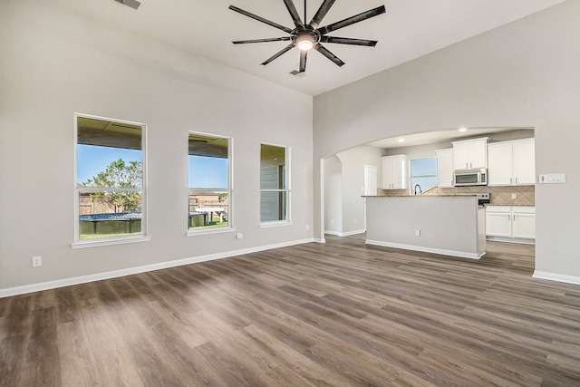 unfurnished living room with a high ceiling, dark hardwood / wood-style floors, ceiling fan, and sink