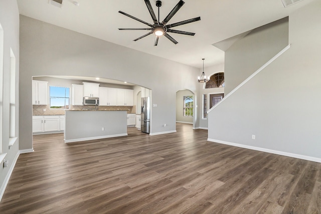 unfurnished living room featuring dark wood-type flooring, a high ceiling, and ceiling fan with notable chandelier