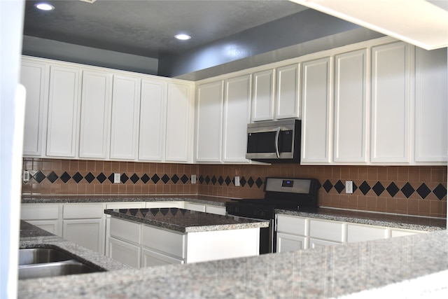 kitchen featuring white cabinetry, appliances with stainless steel finishes, dark stone countertops, a kitchen island, and decorative backsplash