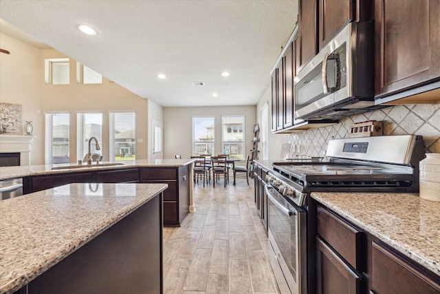 kitchen with appliances with stainless steel finishes, light stone counters, dark brown cabinets, and sink