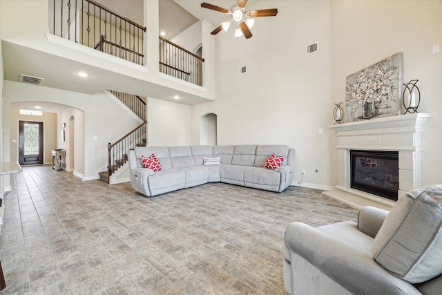 living room with a tile fireplace, ceiling fan, and a high ceiling