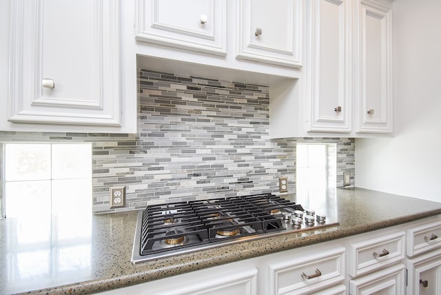 kitchen featuring white cabinets, stainless steel gas cooktop, dark stone counters, and decorative backsplash