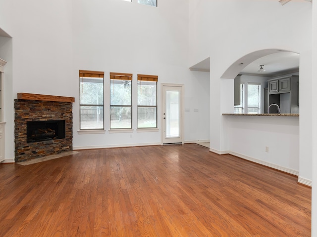 unfurnished living room with a high ceiling, sink, a stone fireplace, and wood-type flooring