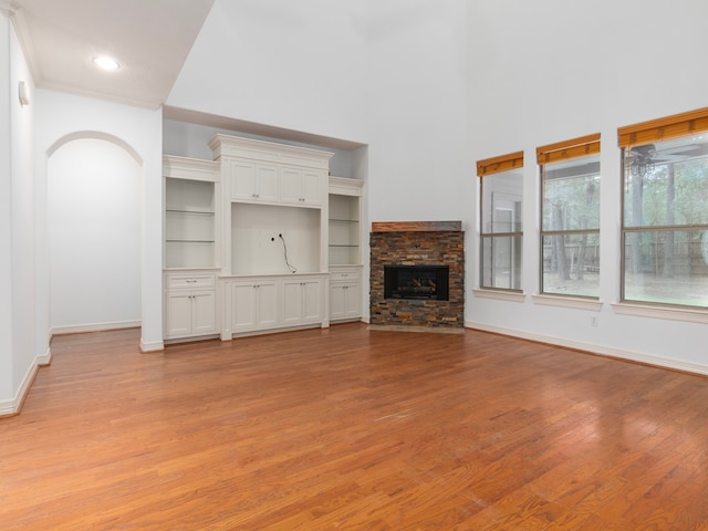 unfurnished living room with a stone fireplace, built in features, and light wood-type flooring