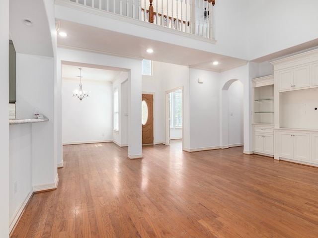 unfurnished living room featuring a towering ceiling, a chandelier, light hardwood / wood-style flooring, and crown molding